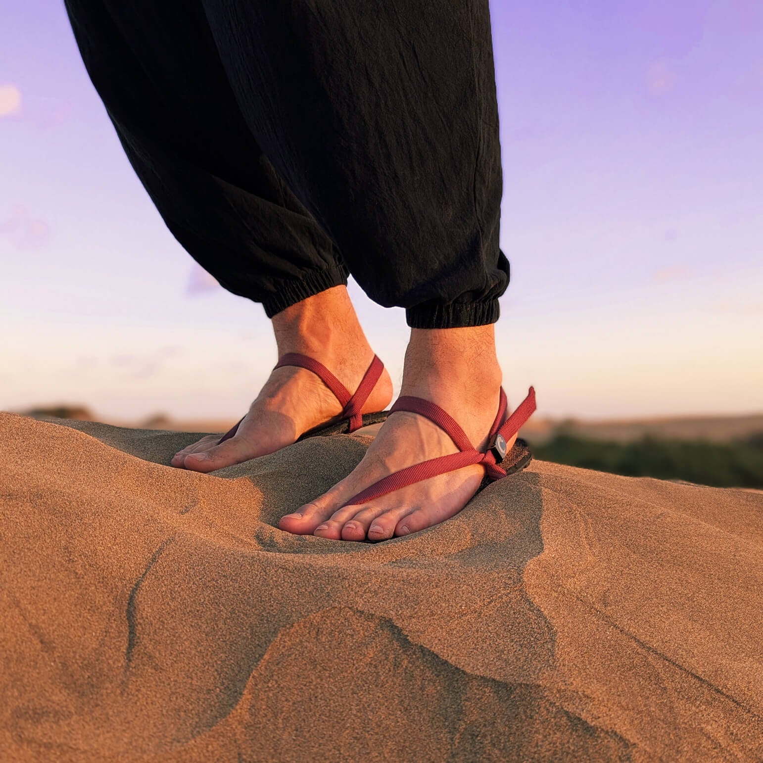 A man in black standing on a dune. Wearing ZuZu Flex barefoot sandals with a urable canvas footbed and burgundy recycled straps. Eco-friendly barefoot adventure sandals